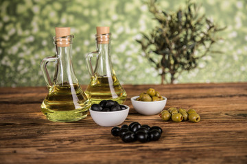Olive oil, olive tree and green and black olives on a wooden table