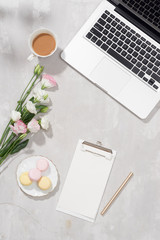 Feminine flat lay workspace with laptop, cup of tea, macarons, lipstick and flowers on white table. Top view mock up.