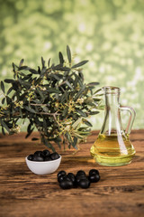 Olive oil and olive tree and black olives and bottles with olive on a wooden table