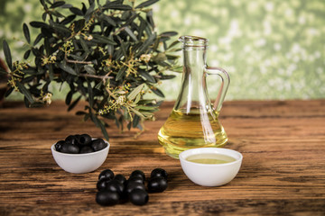 Olive oil and olive tree and black olives and bottles with olive on a wooden table