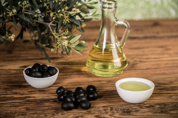 Olive oil and olive tree and black olives and bottles with olive on a wooden table