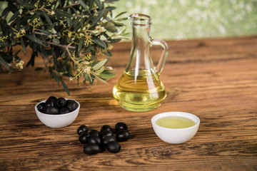 Olive oil and olive tree and black olives and bottles with olive on a wooden table