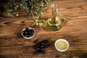 Olive oil and olive tree and black olives and bottles with olive on a wooden table