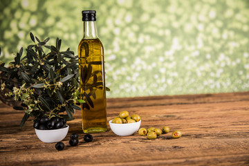 Olive oil, olive tree and green and black olives on a wooden table