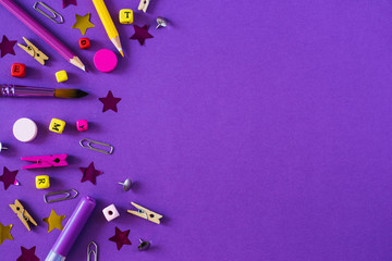 Multicolored school supplies on violet background with copy space.