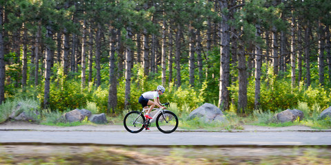 Young Woman Cyclist Riding Road Bicycle on the Free Road in the Forest at Hot Summer Day. Healthy Lifestyle Concept.
