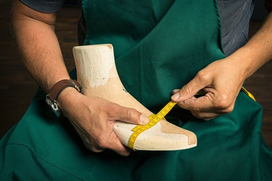 close up of orthopedic shoemaker measuring a wooden last