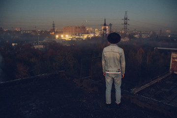 Urban man with hat against the background of the city. Cool guy. Wearing white shirt and jeans. Old neglected building in the background. Shoot from the back.