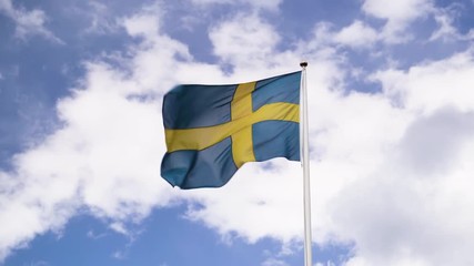 The Swedish flag blowing in the wind. Beautiful blue sky with white clouds.