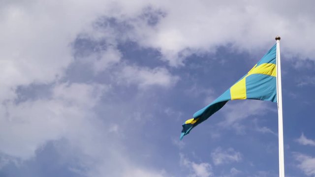 Swedish flag waving in the wind against a blue sky with white clouds.
