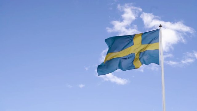 Swedish flag blowing in the wind against a blue sky with white clouds. Slow motion video.