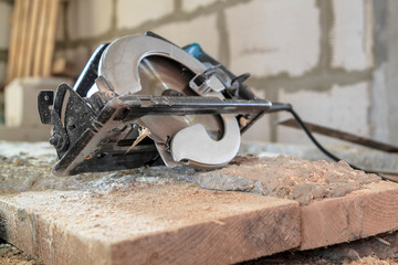 manual circular saw is on a wooden board in house under construction of foam block