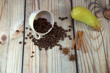 An inverted cup of coffee beans, a ripe green pear, a bunch of cinnamon and star anisets lie on a...