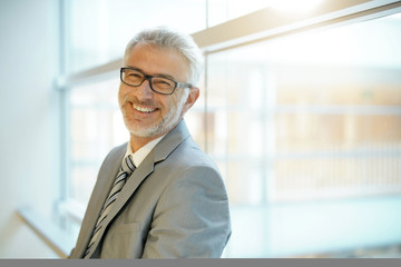Smiling mature businessman leaning on office window smiling at camera