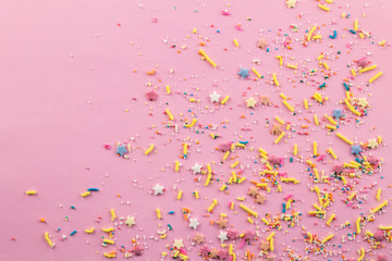 Sprinkles on pink background - Assorted colourful cake topping sprinkles scattered on pink on bottom corner with space for text - top view of star shapes, dots and oblong sprinkles