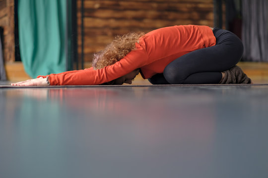 Young woman practicing yoga, doing Child exercise, Balasana pose. Indoor full length. Position for rest and relaxation