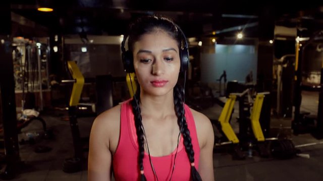 Young Indian female walking on treadmill while listening to music at the gym 