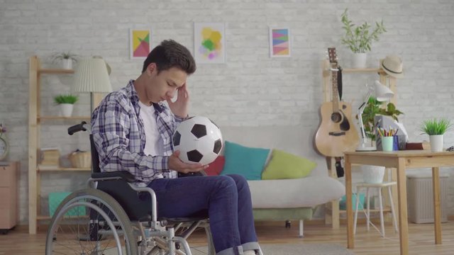 sad young asian man disabled in a wheelchair former athlete football player with a soccer ball