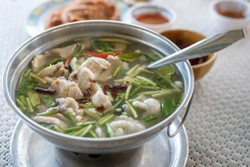 Thai clear spicy hot & sour soup (Tomyum) with boiled asian red tail cat fish fillet and herb usually served in a metal pot heated by a charcoal fire