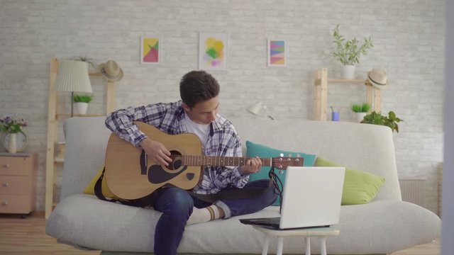 a young Asian man learns to play the guitar depends on the laptop training video