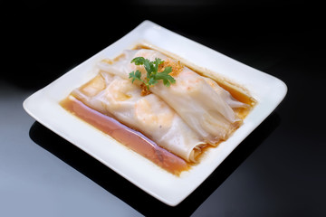 Chinese rice noodle roll with shrimp topping with parsley on white plate over black table at Hong Kong dim sum restaurant