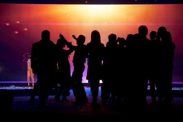 Silhouettes of people dancing and drink over colourful led screen background at nightclub