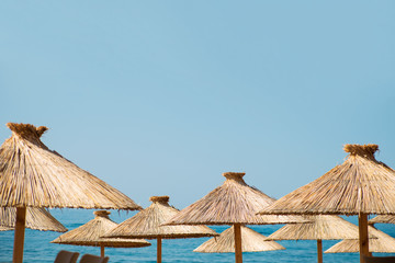 Straw beach umbrellas on a blue sky and sea background with a copy space. Travel, tourism, resort, summer vacation concept