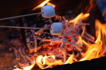 Fototapeta premium two marshmallows on the skewers roasting over the flames at the evening