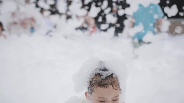 Little girl dancing and having fun in the white foam on a foam party.