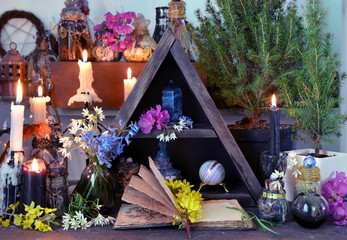 Open book with flowers, candles and magic bottles on witch table.