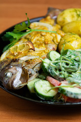 Baked trout with lemon on a plate with arugula, tomato, cucumber salad and young potatoes with dill.