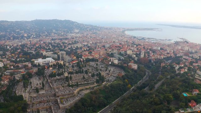 Aerial, tilt up, drone shot, over La Croix des gardes and Cimetiere du grand jas graveyard. overlooking the marina and the mediterranean ocean, on a cloudy day, in Cannes, French Riviera, in France