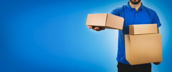 delivery service man holding cardboard boxes on blue background copy space