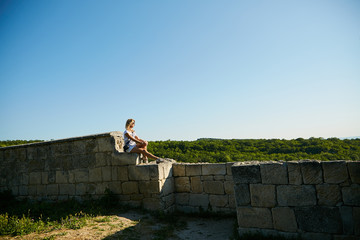 Fototapeta premium A woman sits on an ancient stone wall admiring the scenery of the Crimean peninsula.