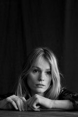 black and white vertical close up headshot of blond woman in studio with melancholic expression on sad face with black background and natural light