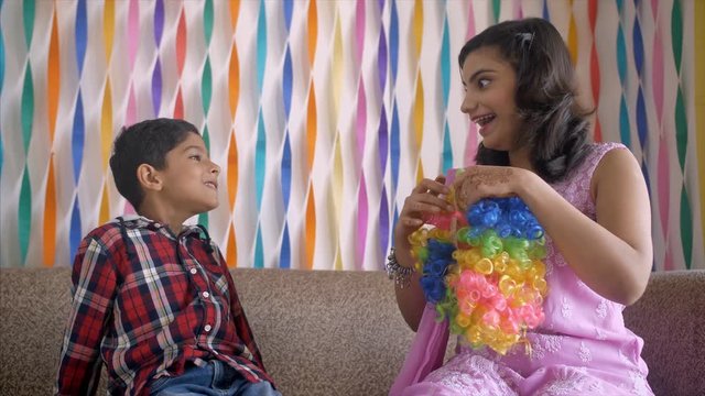 Five-year-old school going naughty kid with a young Indian mother - Mother surprise gift. Young mother surprises her son with a clown cap before his birthday celebration - Decorated walls 