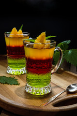 Two glass glasses with fruit jelly on a wooden stand.