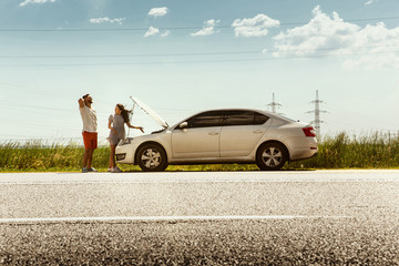 The young couple broke down the car while traveling on the way to rest. They are trying to fix the broken by their own or should hitchhike, getting nervous. Relationship, troubles on the road