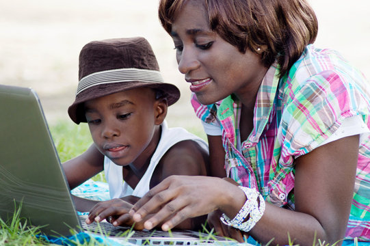 This woman and her son lying on the grass, working with his laptop.