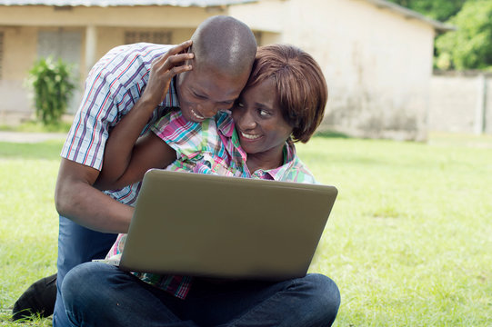 This young couple sitting on the grass, happy working with their laptop.