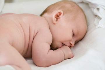 2 month old baby sleeping in frog with hand in mouth.