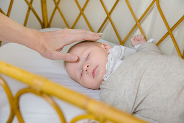 Hand of a mother on the head of her 2 month old baby sleeping on her back in bed.