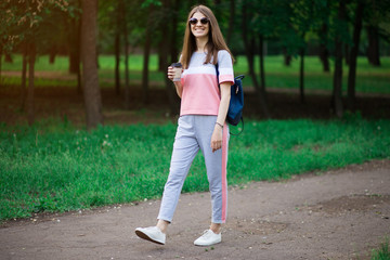 Coffee on go. Beautiful young woman in sunglasses holding coffee cup and smiling while walking along the street