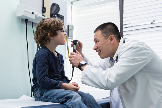 Young asian male doctor examining caucasian boy patient with tool
