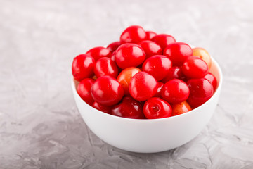 Fresh red sweet cherry in white bowl on gray concrete background. side view.
