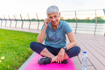 Relaxing after training. Mined and body relaxation in park. Woman on a yoga mat to relax outdoor. Senior woman resting on mat after exercise