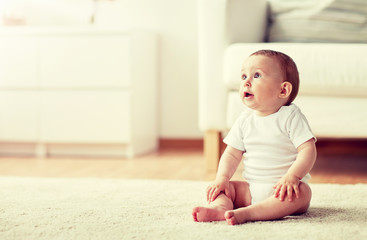 childhood, babyhood and people concept - happy little baby boy or girl sitting on floor at home