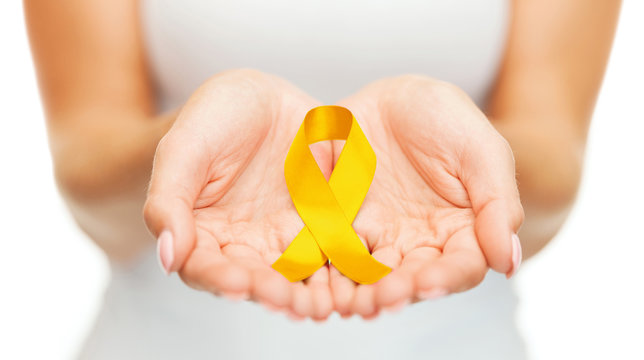 healthcare, charity and medicine concept - close up of woman cupped hands holding yellow gold childhood cancer awareness ribbon