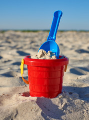 Baby red plastic bucket with sand and shovel on the seashore © nndanko
