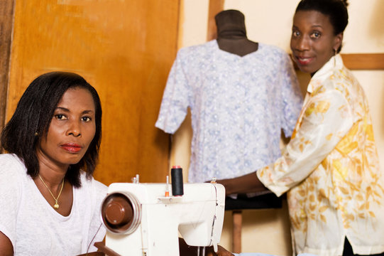 Young seamstress in front of her sewing machine while her colleague dresses the mannequin.